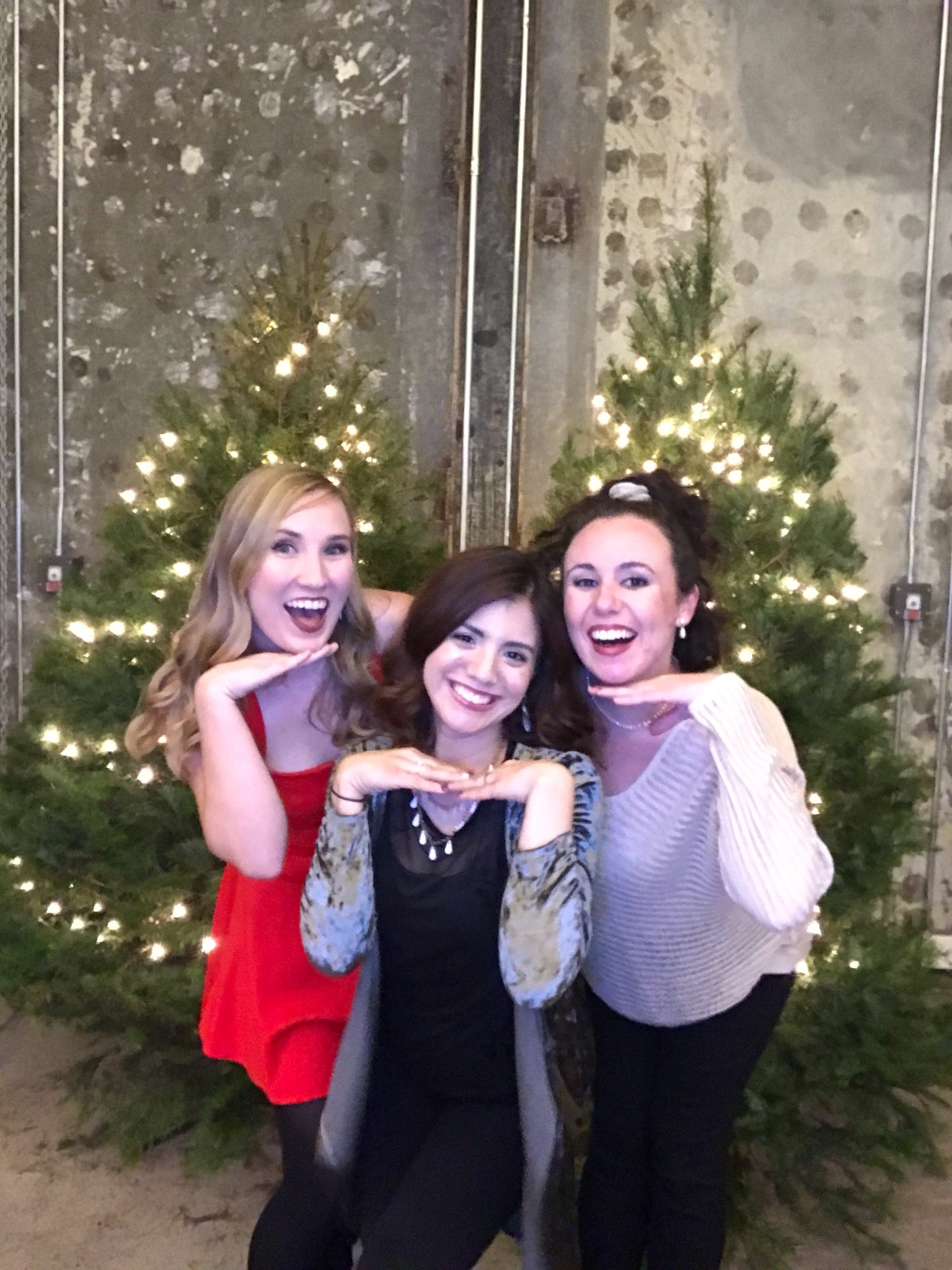 Tres invitados sonríen junto a árboles navideños en una foto de iPad