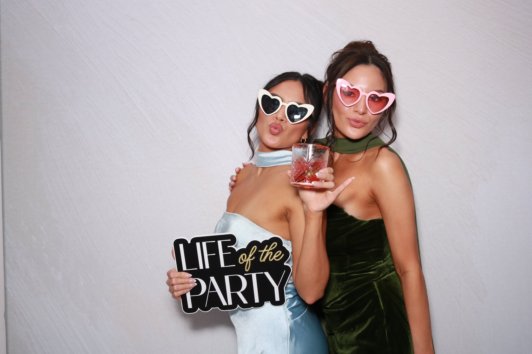 Two guests posing together with sunglasses and a celebration sign